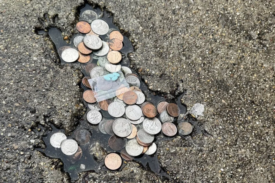 Rat shaped indentation on pavement, filled with coins
